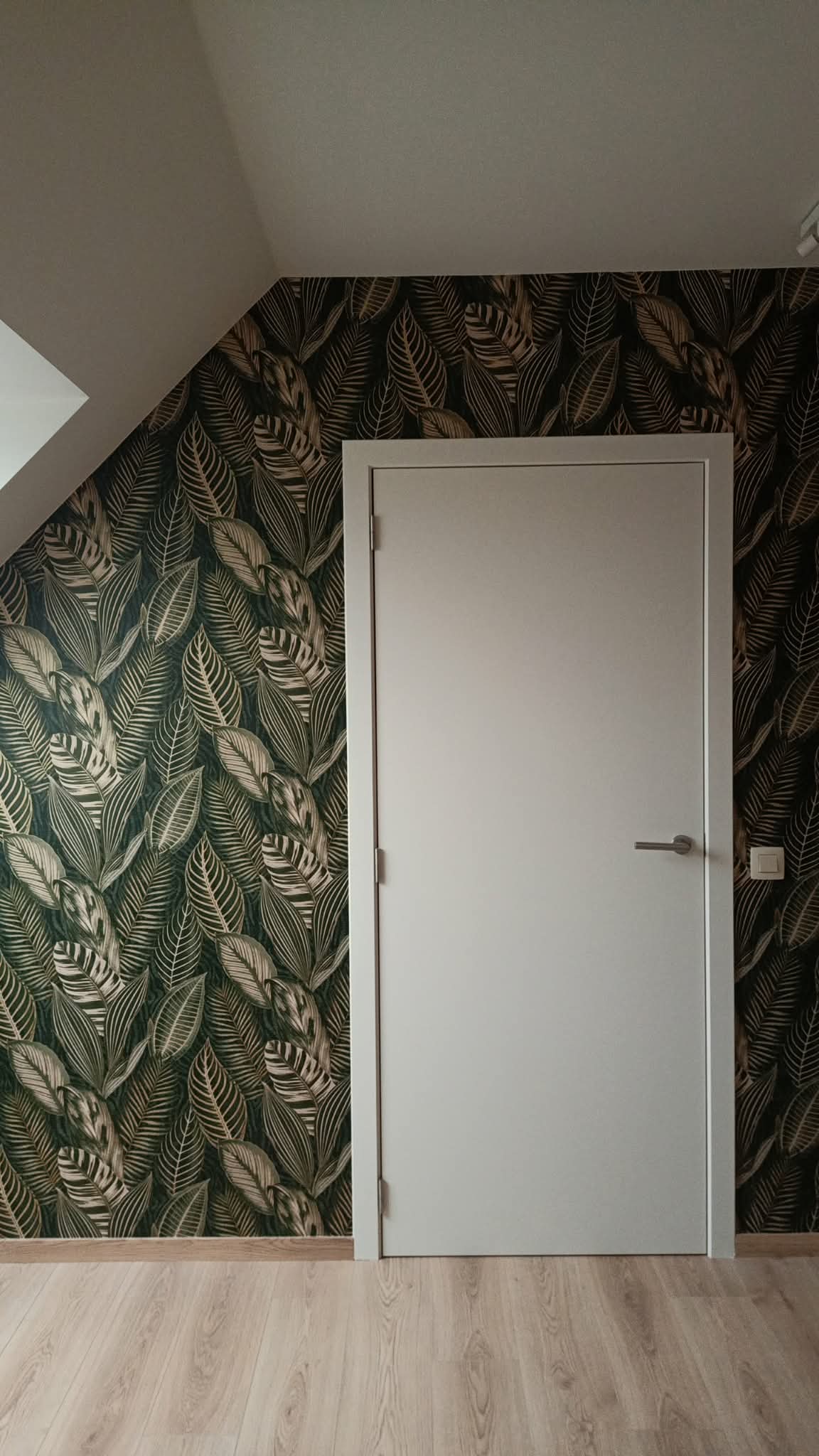 Porte blanche moderne sur un mur tapissé de motifs de feuilles tropicales vertes et dorées.